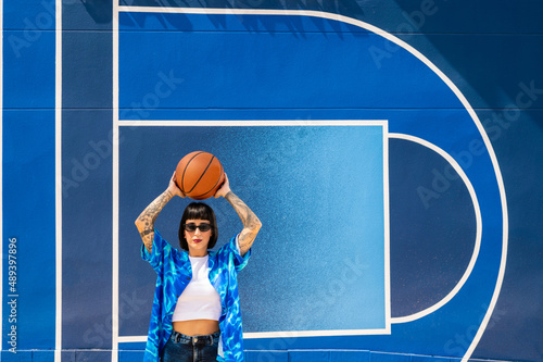 Una mujer caucásica con tatuajes y pelo corto en una pista deportiva con un balón de baloncesto 