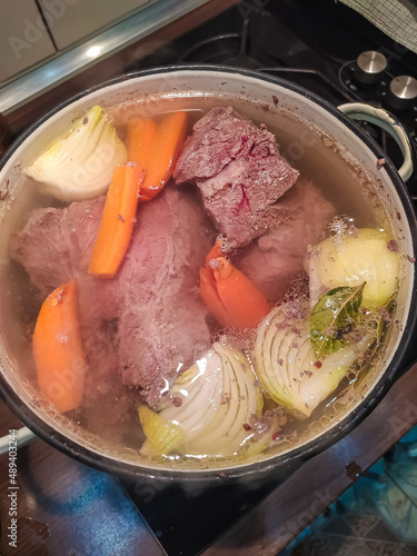 Large chunks of meat are boiled with onions and carrots in a large saucepan. The process of cooking jelly. Ingredients for meat soup. Top view