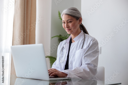Focused woman medical specialist typing on laptop sitting at office