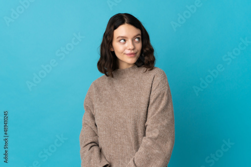 Teenager Ukrainian girl isolated on blue background having doubts while looking up