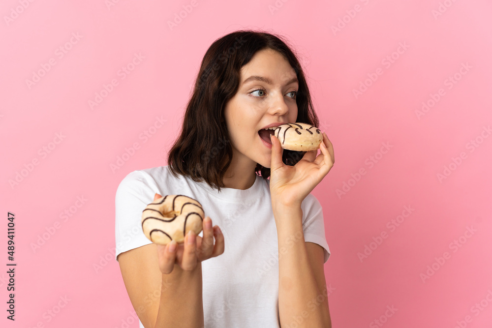 Teenager Ukrainian girl isolated on pink background eating a donut Teenager Ukrainian girl isolated on pink background eating a donut