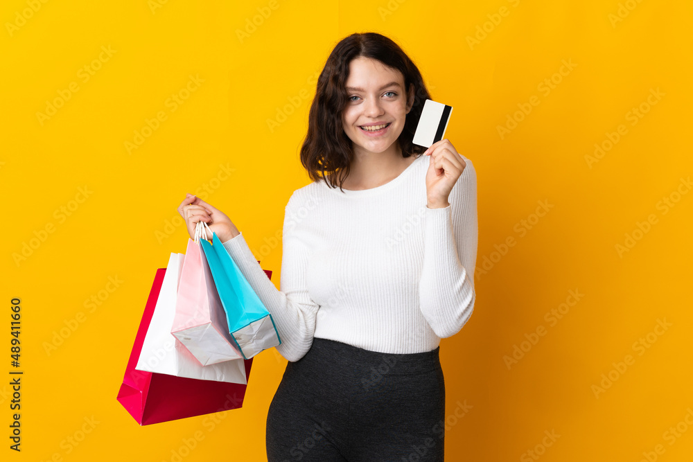 Teenager Ukrainian girl isolated on yellow background holding shopping bags and a credit card Teenager Ukrainian girl isolated on yellow background holding shopping bags and a credit card