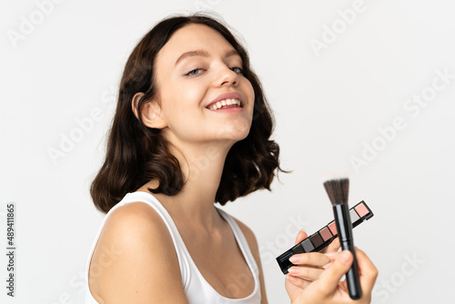Teenager Ukrainian girl isolated on white background with makeup palette and happy