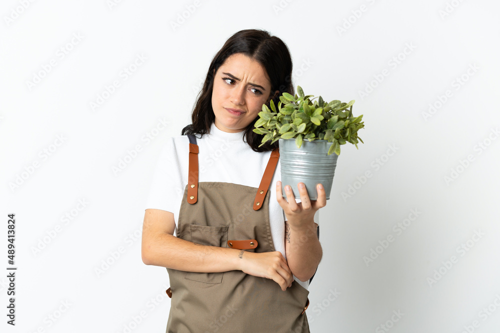 Young caucasian woman holding a plant isolated on white background with sad expression Young caucasian woman holding a plant isolated on white background with sad expression