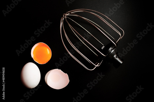whisk for whipping and broken eggs in the shell on a black background