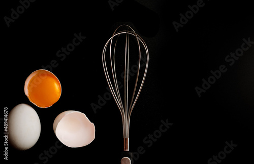 whisk for whipping and broken eggs in the shell on a black background