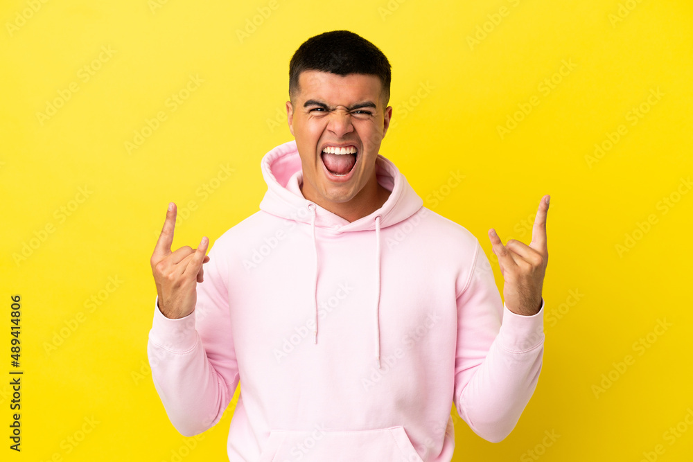 Young handsome man over isolated yellow background making horn gesture Young handsome man over isolated yellow background making horn gesture