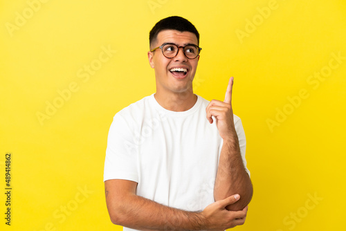 Young handsome man over isolated yellow background pointing up a great idea