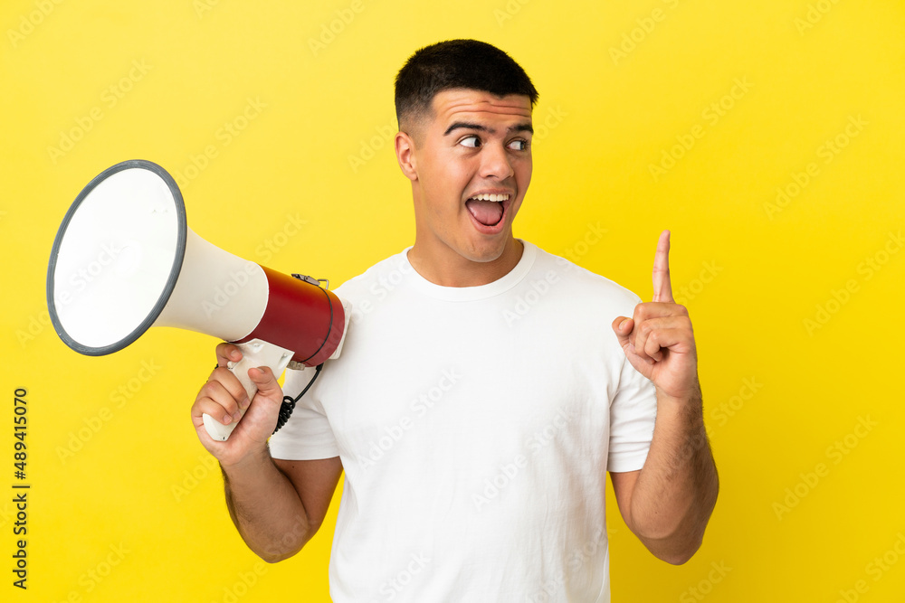 Young handsome man over isolated yellow background holding a megaphone and intending to realizes the solution Young handsome man over isolated yellow background holding a megaphone and intending to realizes the solution