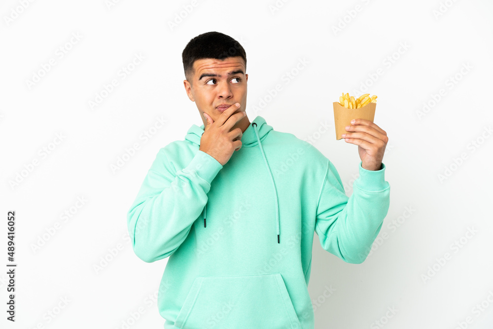 Young handsome man holding fried chips over isolated white background having doubts Young handsome man holding fried chips over isolated white background having doubts