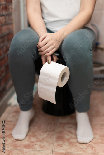 woman sitting on the toilet holding a roll of paper