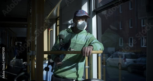 Man with a breathing mask and a skateboard in a moving tramway. Head close to the window in sunny weather.