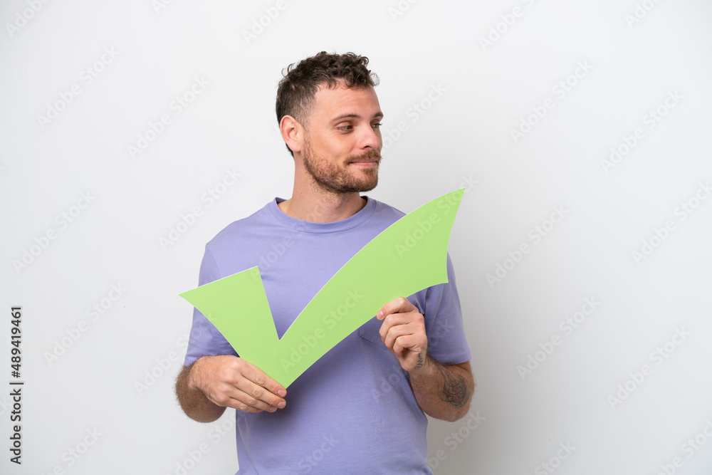 Young Brazilian man isolated on white background holding a check icon and looking side Young Brazilian man isolated on white background holding a check icon and looking side