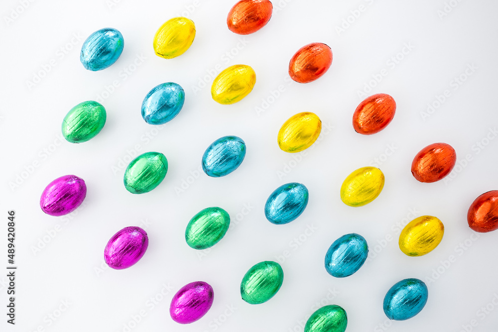 Easter holiday greeting card with geometric pattern design. Small chocolate eggs wrapped in colorful foil as rainbow lgbtq pride flag. Isolated on white background, copy space. Easter holiday greeting card with geometric pattern design. Small chocolate eggs wrapped in colorful foil as rainbow lgbtq pride flag. Isolated on white background, copy space.