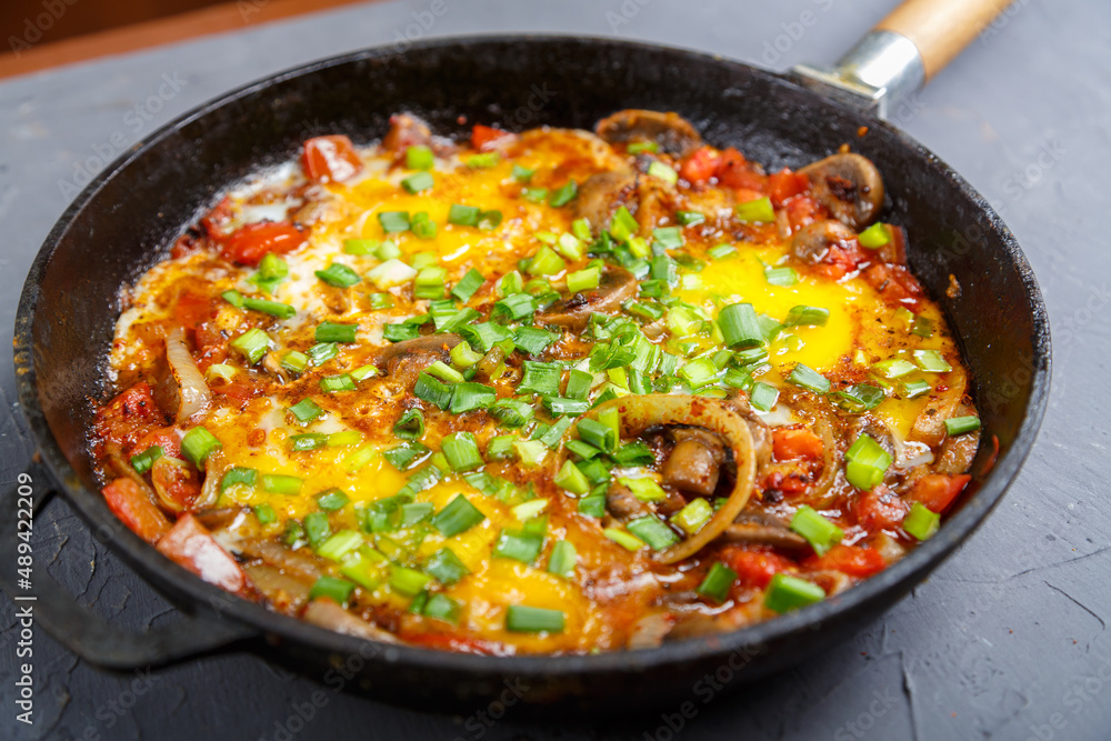 Shakshuka hot with herbs in a frying pan on a gray table. Shakshuka hot with herbs in a frying pan on a gray table.