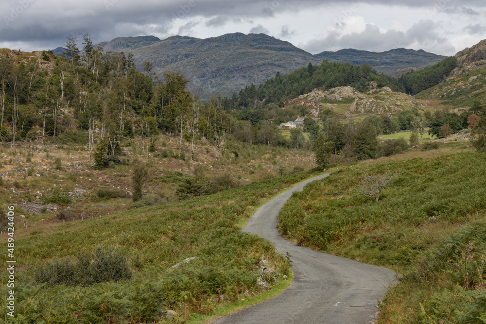 Country road in the Lake District, close to Seathwaite, winds its way through the upland hills and vegetation with Ulpha Fell and Cold Pike in the distance
