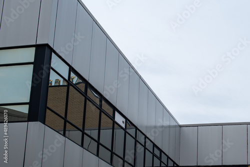 The exterior wall of a contemporary commercial style building with aluminum metal composite panels and glass windows. The futuristic building has engineered diagonal cladding steel frame panels.