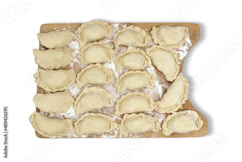 Raw pierogi stuffed with white cheese lying on wooden kitchen board on white isolated background. Traditional Polish dish.