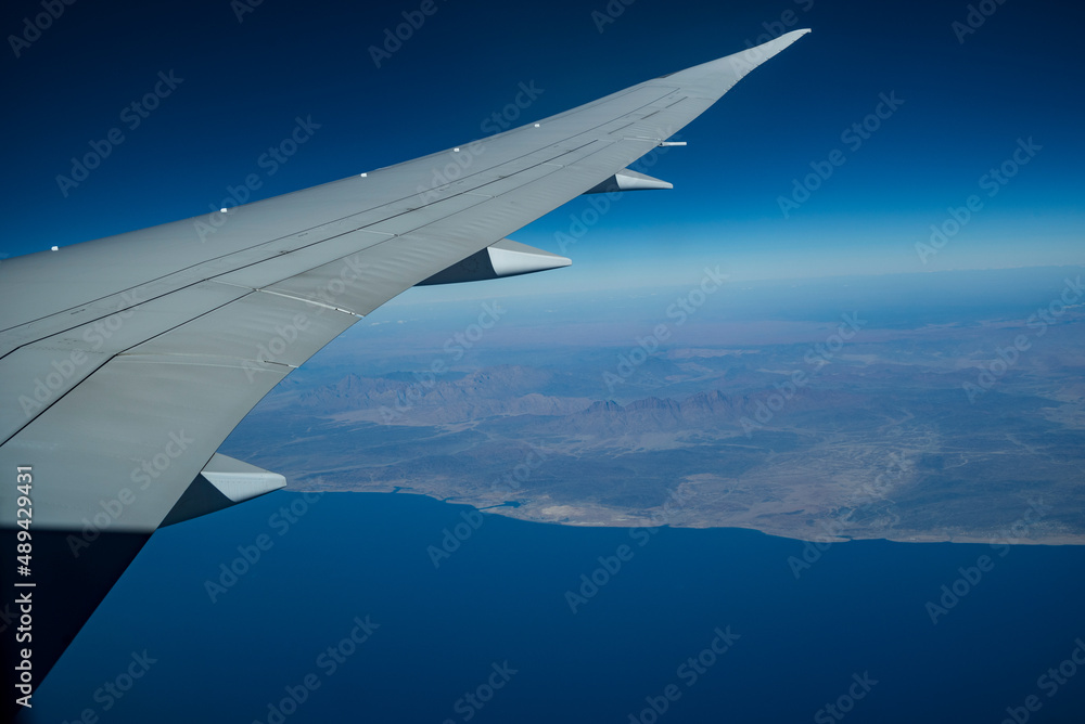 Airplane wing seen from the window, in the background the west coast of the Arabian Peninsula, Red Sea