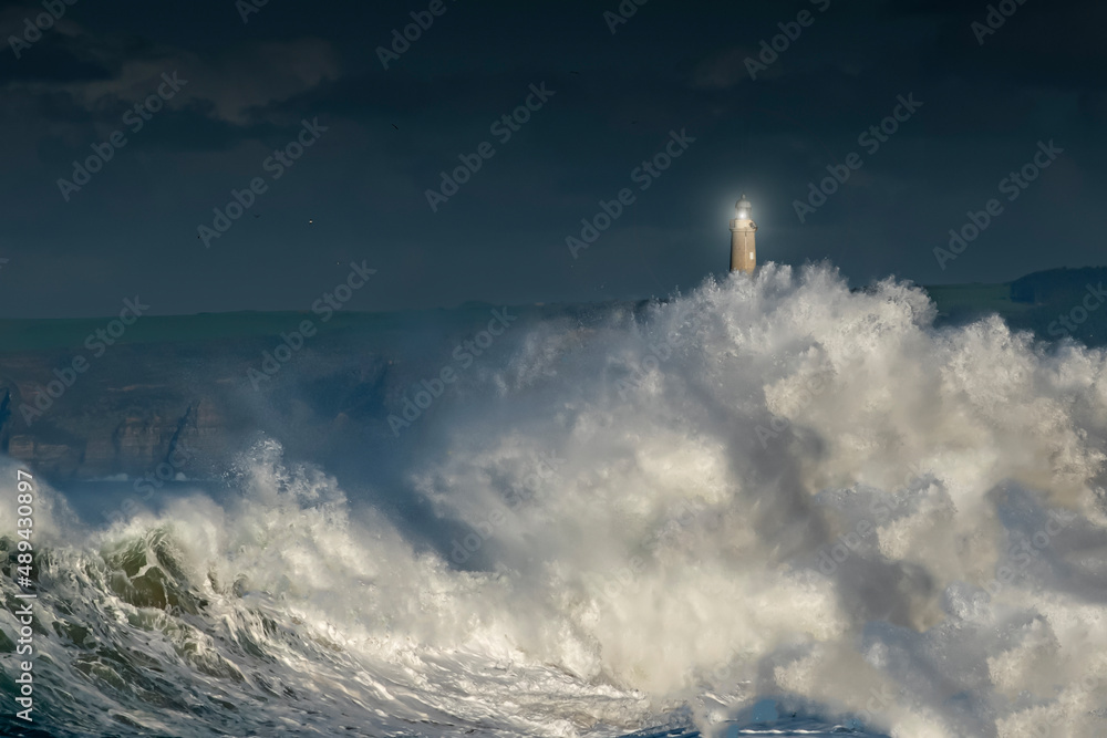 olas gigantes en la costa cantábrica con un faro alumbrando en la tempestad