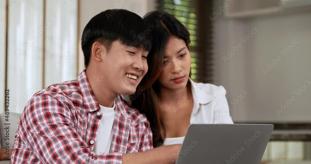 Slow motion shot, Happy Young couple sitting on sofa in living room at home use laptop computer working, talking and smile together with happiness, happy family concept Slow motion shot, Happy Young couple sitting on sofa in living room at home use laptop computer working, talking and smile together with happiness, happy family concept