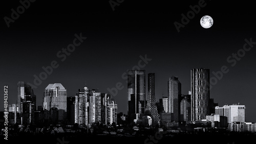 Black and white cityscape. Last full moon of 2021 setting over the Calgary Alberta city skyline lit by the rising sun. copy space