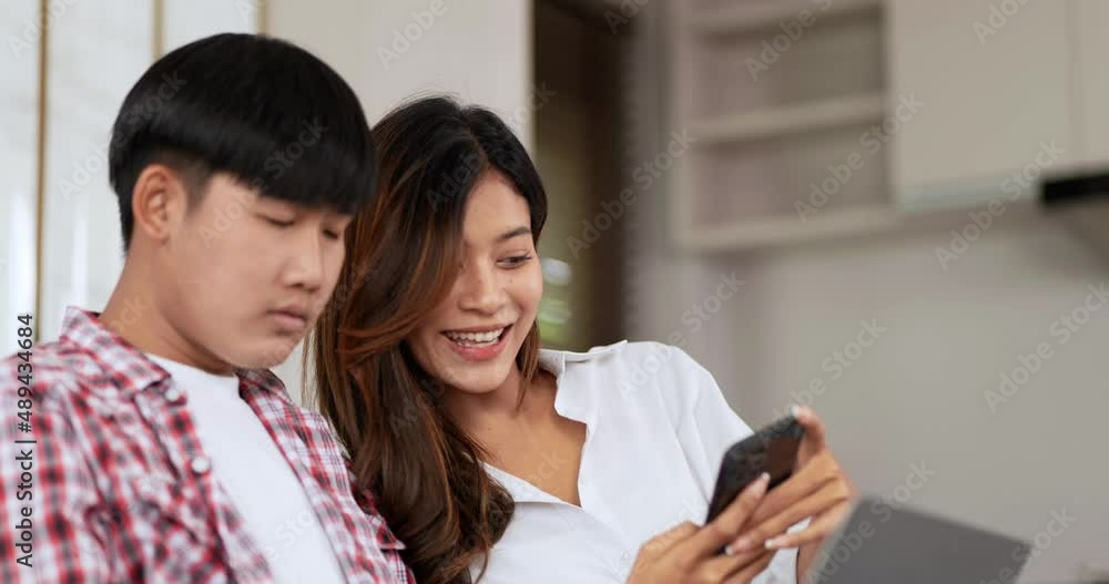 Attraction Young couple sitting on sofa in living room, young man use laptop, Beautiful woman show her smartphone display to young man, he was disinterested Attraction Young couple sitting on sofa in living room, young man use laptop, Beautiful woman show her smartphone display to young man, he was disinterested
