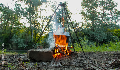 Fototapeta Naklejka Na Ścianę i Meble -  Cooking on a campfire in nature, cooking on a campfire in the campaign. Camp kitchen, cooking in the forest on a fire. Pot on an open fire. The concept of camping life.