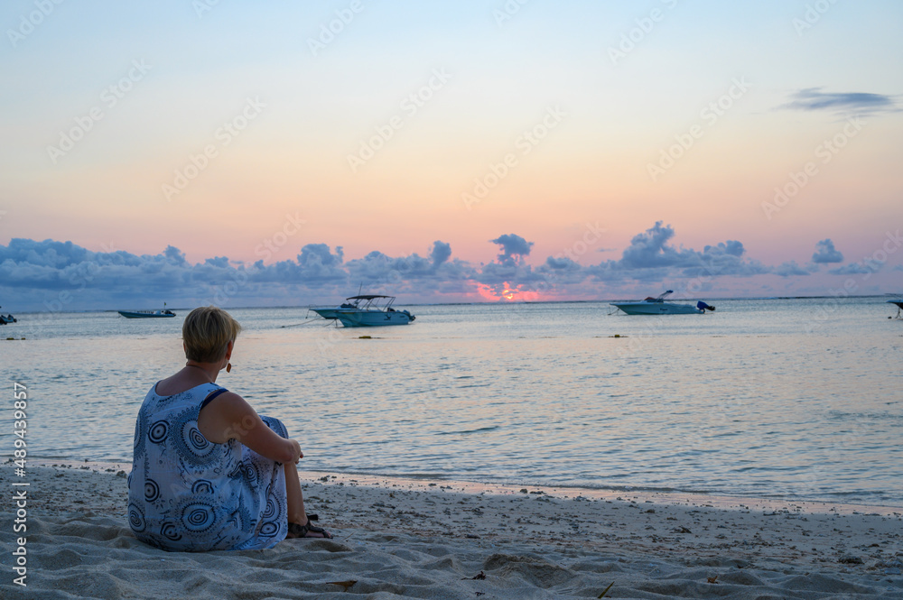 Woman sitting on beach at sunset