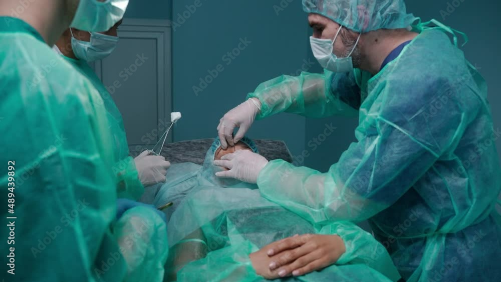 Surgeons and nurses performing rhinoplasty in green protective gowns. Slow-motion process of rhinoplasty surgeon process. Surgeon hands surgical scissors to nurse. High quality 4k footage Surgeons and nurses performing rhinoplasty in green protective gowns. Slow-motion process of rhinoplasty surgeon process. Surgeon hands surgical scissors to nurse. High quality 4k footage