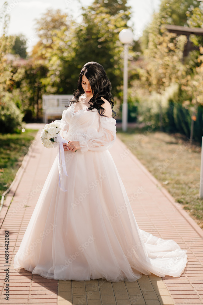 brunette bride in a dress with a bouquet of flowers on the path in the park. brunette bride in a dress with a bouquet of flowers on the path in the park.
