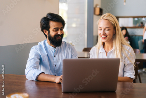 Close-up front view of two multiracial smiling creative workers discussing project during meeting in cafe. Portrait of young business people having successful meeting at restaurant, selective focus.