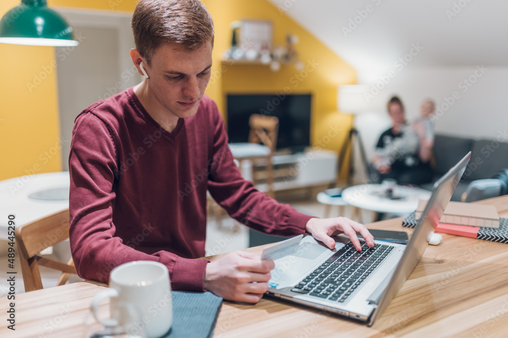 Redhead man using a laptop and his credit card at home Redhead man using a laptop and his credit card at home