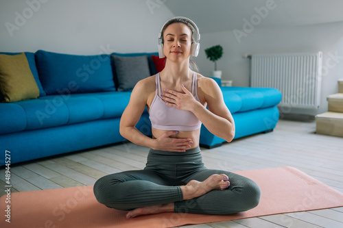 Woman in a lotus position practicing yoga at home and using headphones