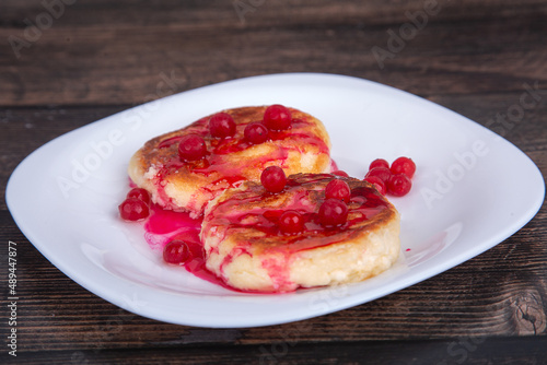 fried cheesecakes with red cherry syrup and cranberries, on a white plate