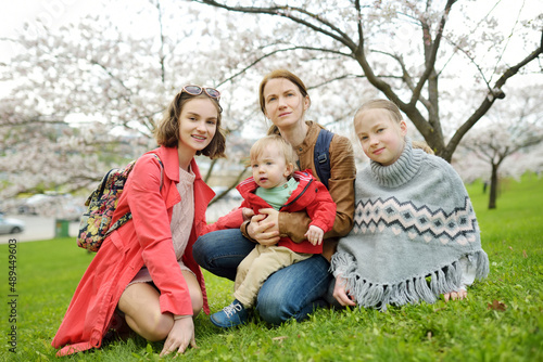 Young mother and het three kids having fun in blooming cherry tree garden on beautiful spring day. Family of four outdoors. © MNStudio
