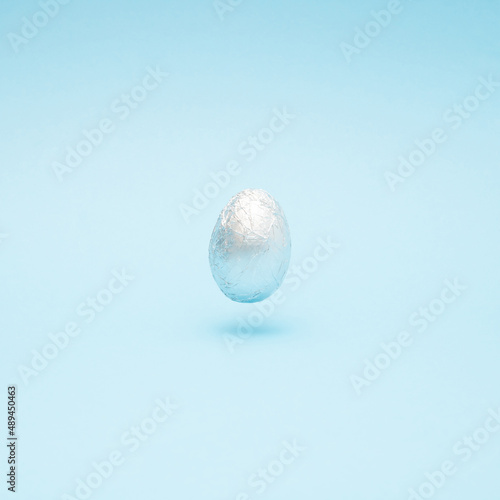 Easter creative layout made with silver Easter egg levitating on a pastel blue background. Minimal holiday still life concept.