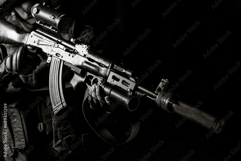 Fototapeta premium Man in black uniform aiming with silenced Kalashnikov assault rifle on black background