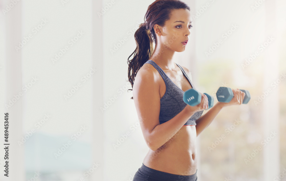 Building her biceps. Cropped shot of an attractive young woman working out with dumbbells in her home.