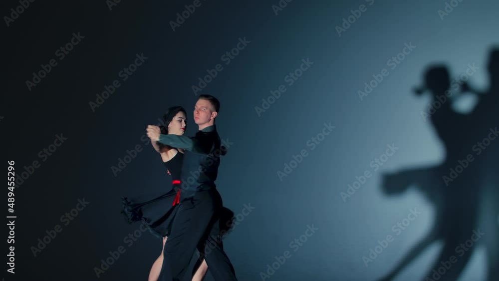 Tango dance performed by pair of ballroom dancers. Man and woman practice elements of Latin choreography. Shot against gray background with dancing shadows. Close up. Slow motion ready, 4K, 59.94fps. Tango dance performed by pair of ballroom dancers. Man and woman practice elements of Latin choreography. Shot against gray background with dancing shadows. Close up. Slow motion ready, 4K, 59.94fps.