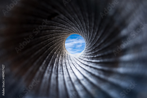 A view through a dark barrel of cannon to the blue sky with white fluffy clouds. Close up, selective focus. Abstract background concept