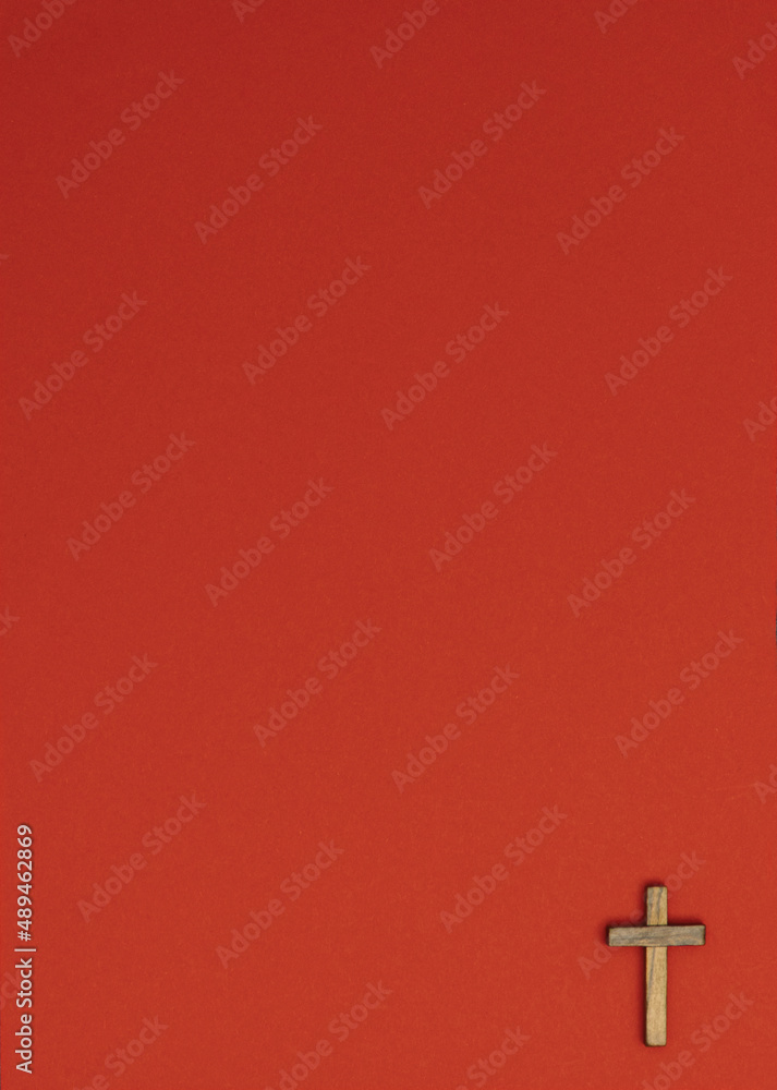 Image of a wooden cross on a red paper background. Flat lay, top view, minimal concept.