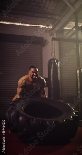 A Vertical Video Of A Hispanic Bodybuilder Tyre Flipping In An MMA Gym. Shot In A Crossfit Boxing Gym With Low Key Lighting And A Scattering Of Haze. Captured On Red Digital Cinema Camera 
