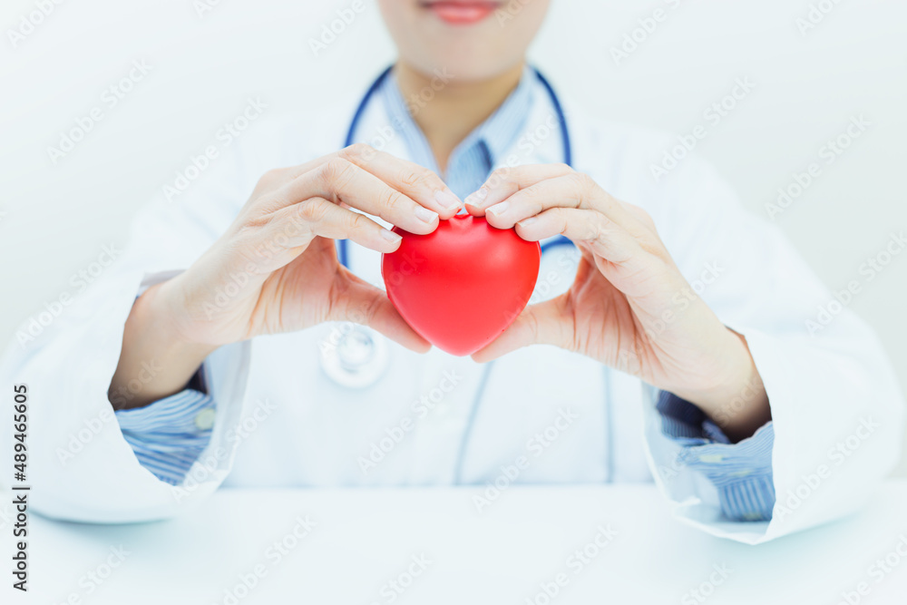 Health insurance and retirement concept / female doctor holding a red heart on the background of the hospital Health insurance and retirement concept / female doctor holding a red heart on the background of the hospital