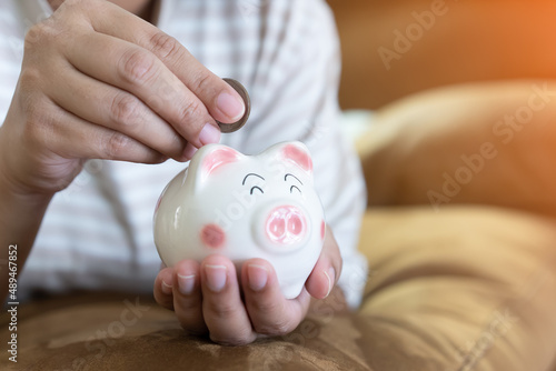 Woman hands holding and putting Thai currency coin into piggy bank. Saving concept with piggy bank indoor with sun light.