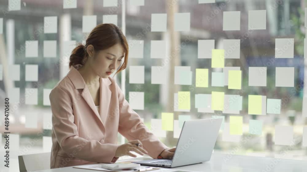 Happy young Asian businesswoman sitting on her workplace in the office. Young woman working at laptop in the office. Happy young Asian businesswoman sitting on her workplace in the office. Young woman working at laptop in the office.