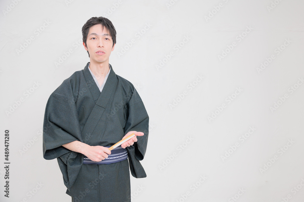 扇子を持って手に当てる着物を着た日本人男性