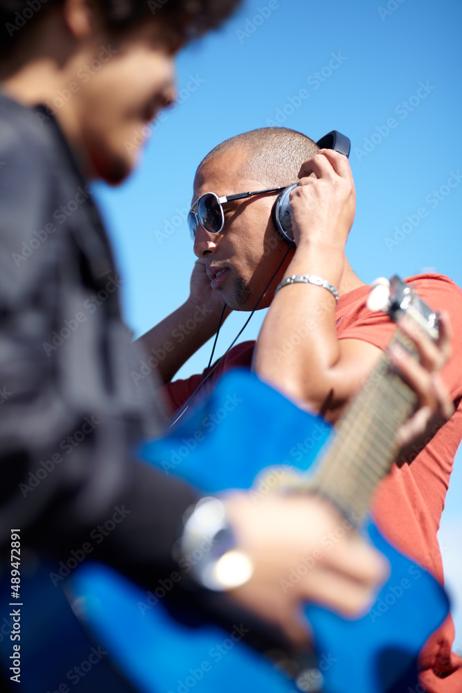 Letting the music lead us. Shot of a young man playing the guitar while his friend uses his his headphones. Letting the music lead us. Shot of a young man playing the guitar while his friend uses his his headphones.