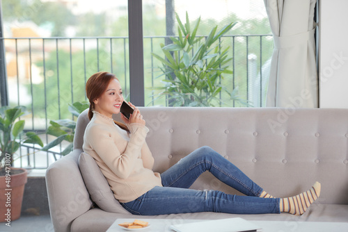 happy smiling asian young woman sitting on sofa and having video call on smartphone at home