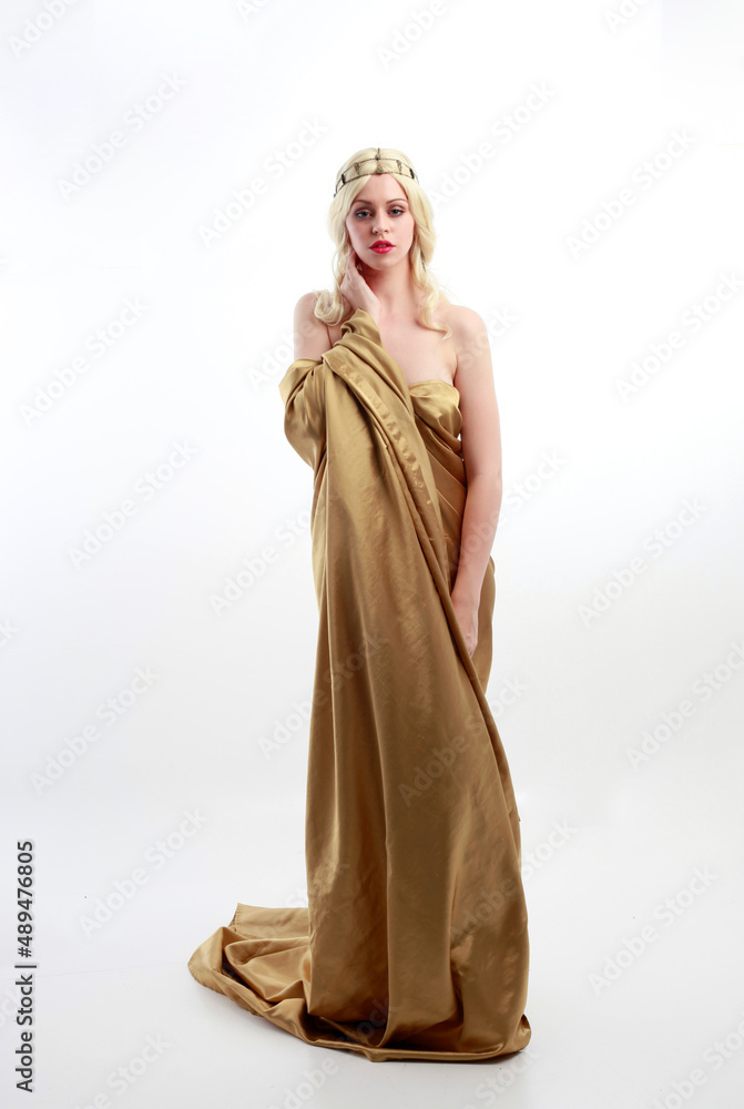 Naklejka premium Full length portrait of pretty female model wearing grecian goddess toga gown, posing with elegant gestural movements on a studio background.